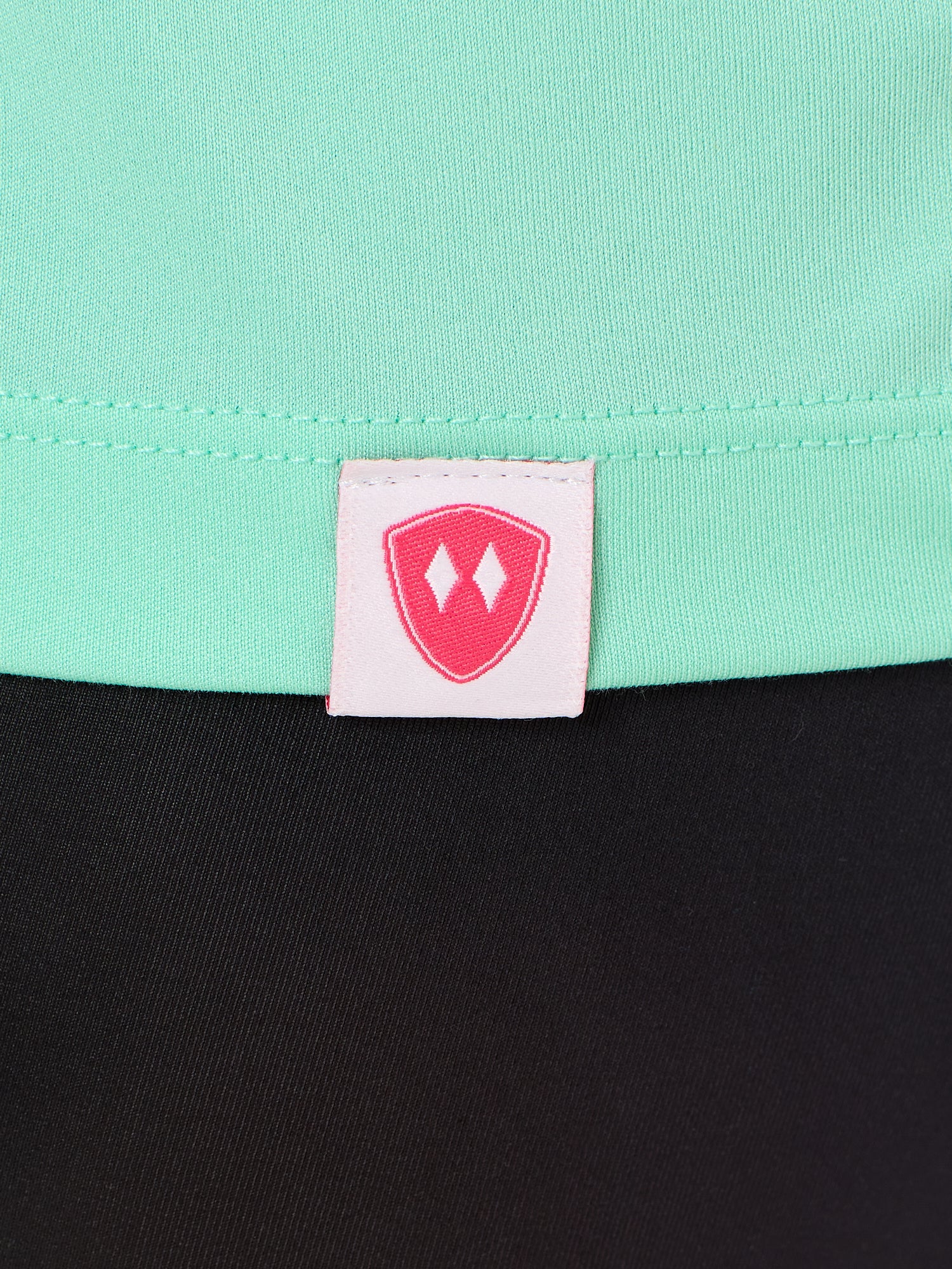 Close-up detail of a pink Double Diamond Shield woven hem label on a mint green performance long sleeve shirt.