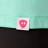 Close-up detail of a pink Double Diamond Shield woven hem label on a mint green performance long sleeve shirt.