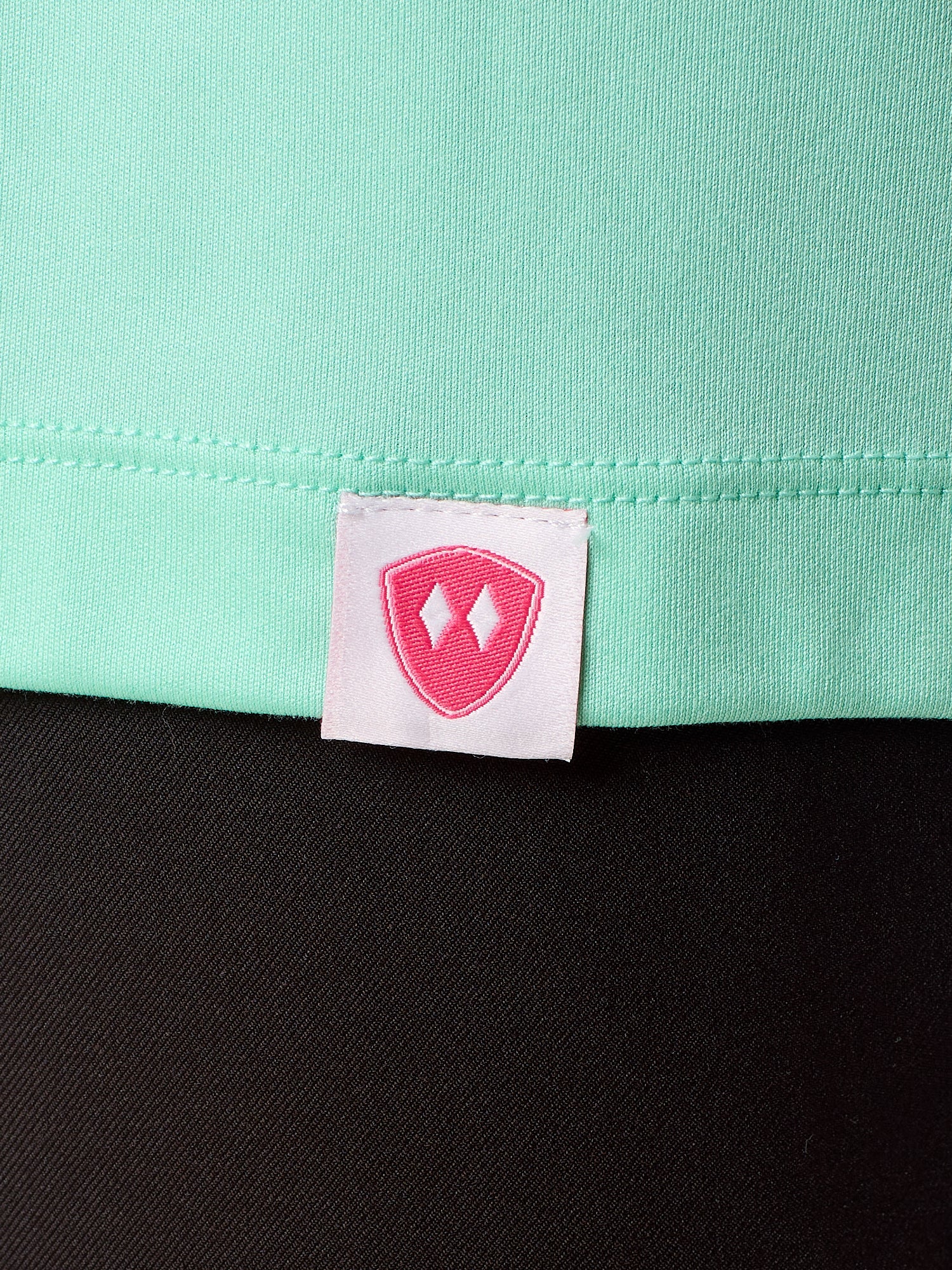 Close-up detail of a pink Double Diamond Shield woven hem label on a mint green performance long sleeve shirt.