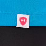 Close-up detail of a pink Double Diamond Shield woven hem label on a sapphire blue performance long sleeve shirt.