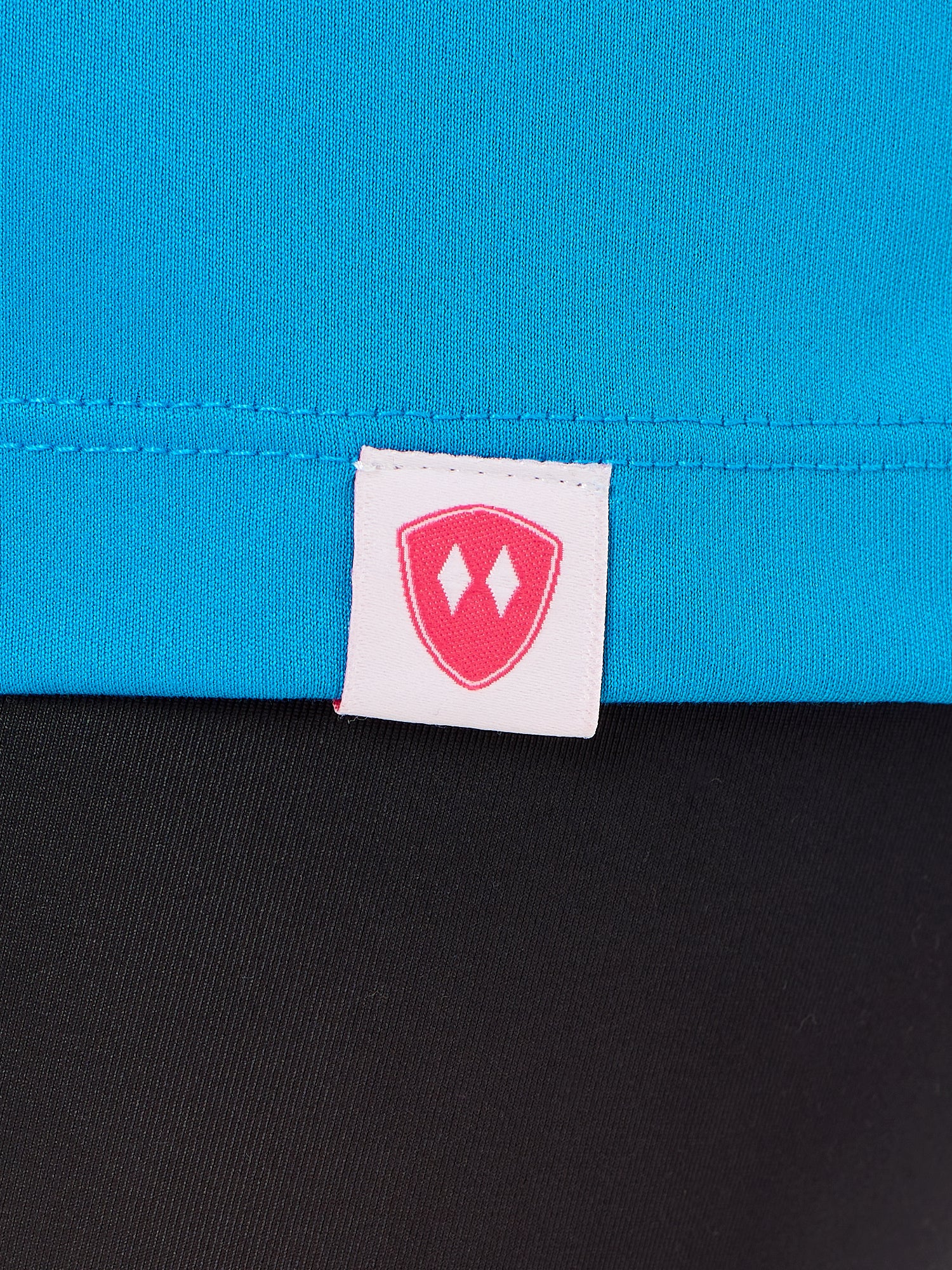 Close-up detail of a pink Double Diamond Shield woven hem label on a sapphire blue performance long sleeve shirt.