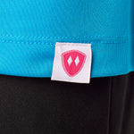 Close-up detail of a pink Double Diamond Shield woven hem label on a sapphire blue performance long sleeve shirt.
