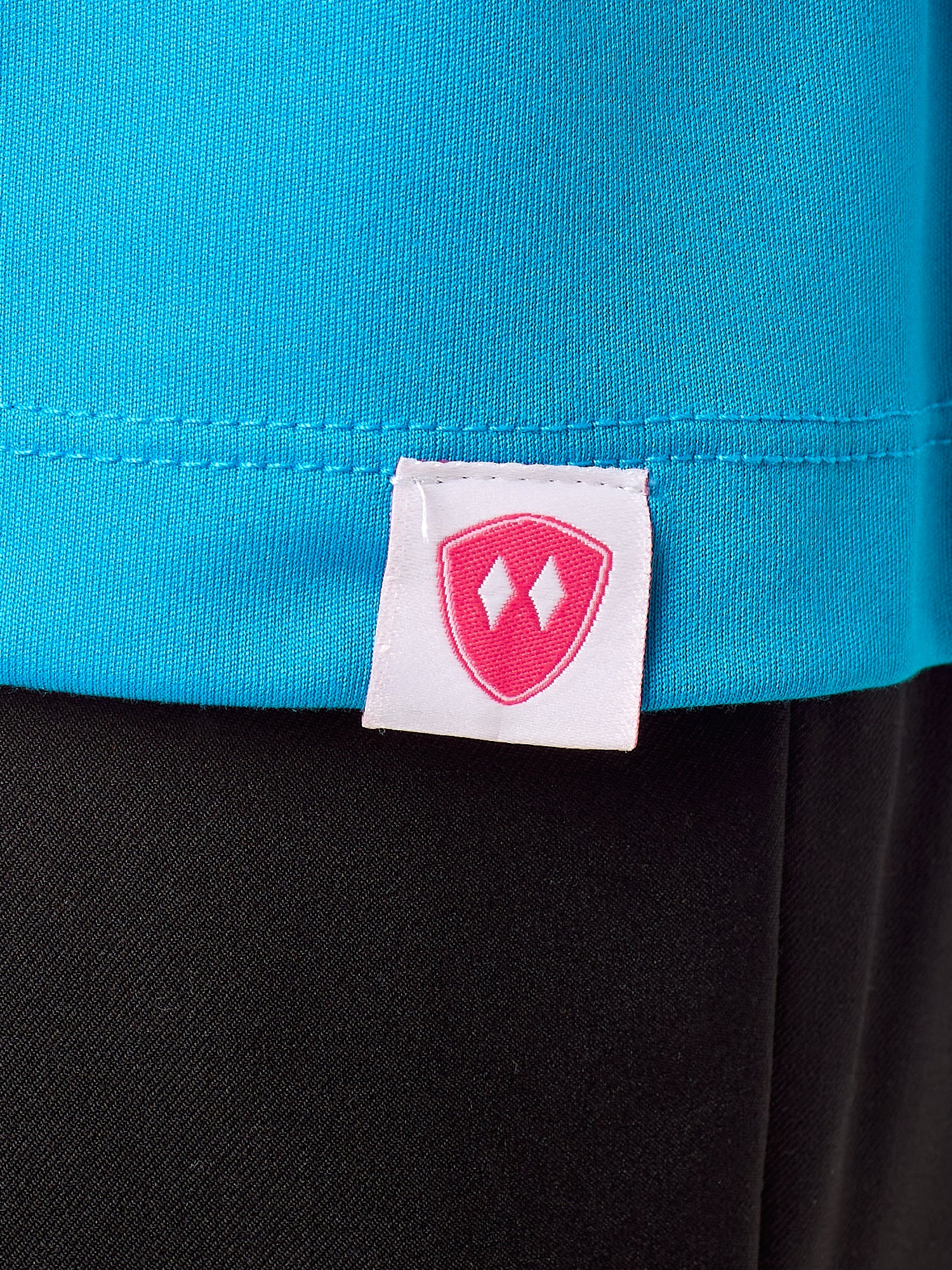 Close-up detail of a pink Double Diamond Shield woven hem label on a sapphire blue performance long sleeve shirt.