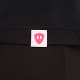 Close-up detail of a pink Double Diamond Shield woven hem label on a black performance long sleeve shirt.