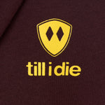 Detail of the yellow till i die logo on an Oxblood hoodie