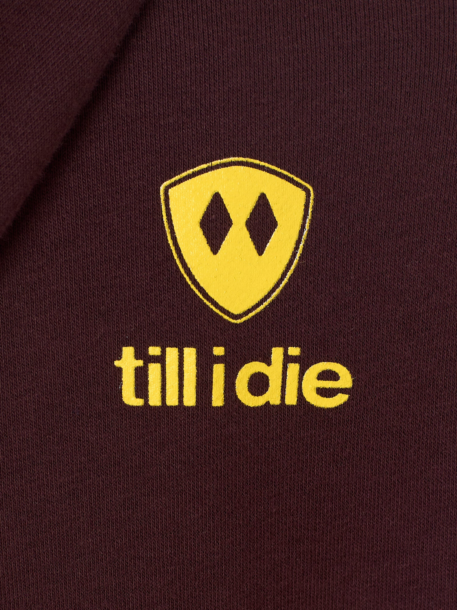 Detail of the yellow till i die logo on an Oxblood hoodie