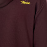 Detail of the yellow till i die logo on an Oxblood hoodie