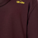 Detail of the yellow till i die logo on an Oxblood hoodie