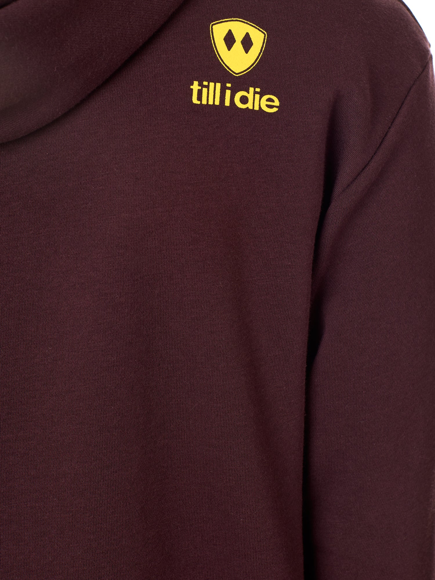 Detail of the yellow till i die logo on an Oxblood hoodie