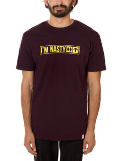 Front view of a male model wearing the "I'm Nasty" Oxblood Tee Shirt. The graphic features trail sign-inspired "I'm Nasty" text with a double diamond symbol indicating expert terrain.