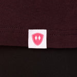 Close-up detail of a pink Double Diamond Shield woven hem label on a Oxblood tee shirt.