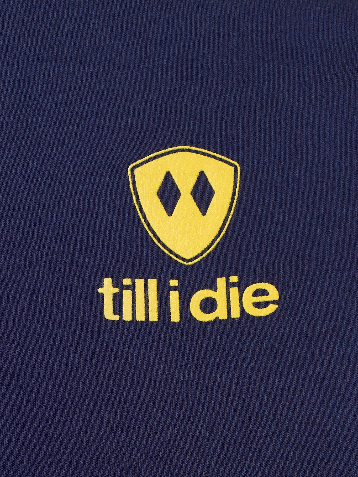 Detail of the yellow till i die logo on a navy tee shirt
