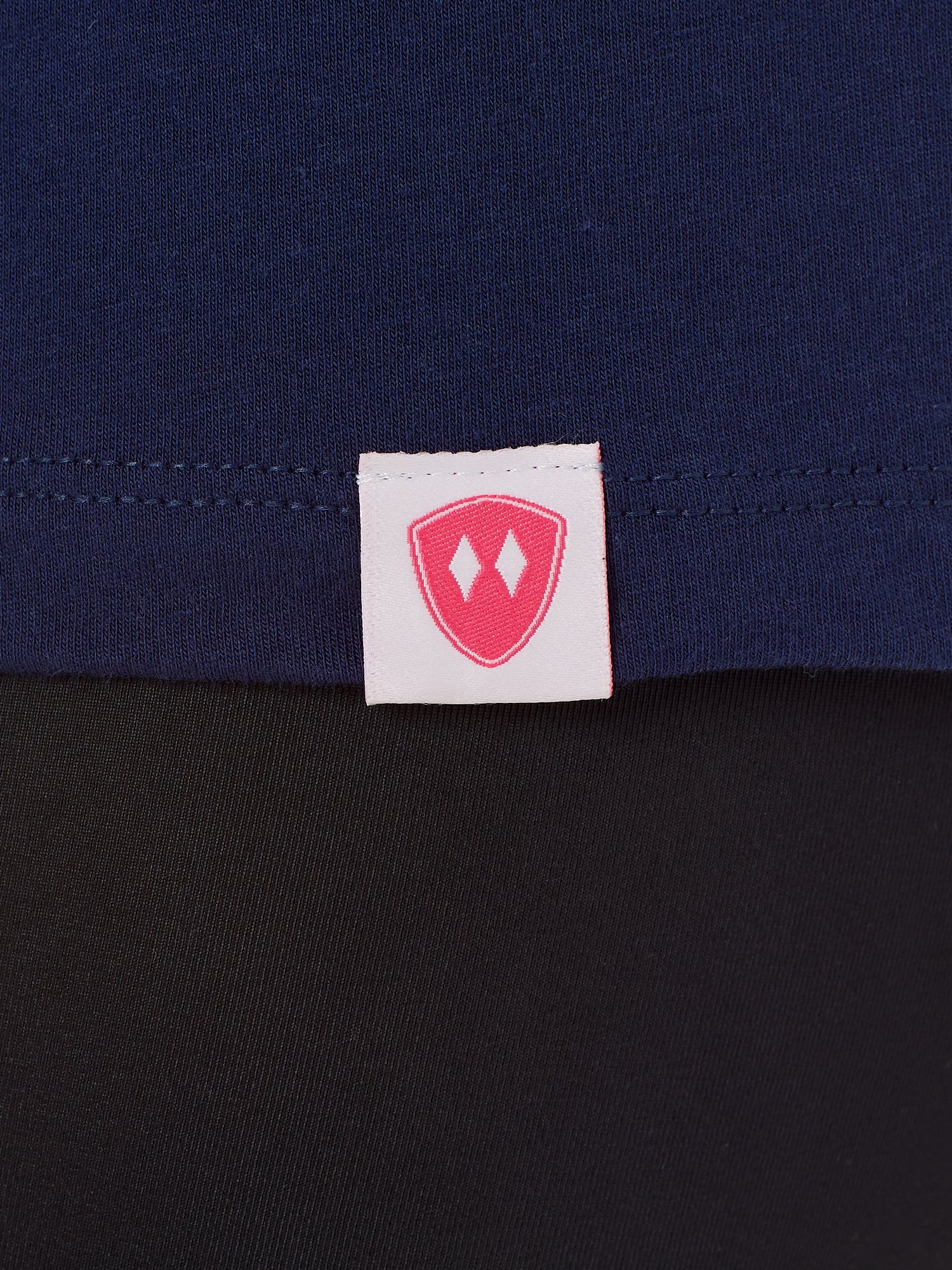 Close-up detail of a pink Double Diamond Shield woven hem label on a Navy Tee shirt.
