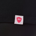 Close-up detail of a pink Double Diamond Shield woven hem label on a black performance long sleeve shirt.