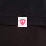 Close-up detail of a pink Double Diamond Shield woven hem label on a black performance long sleeve shirt.
