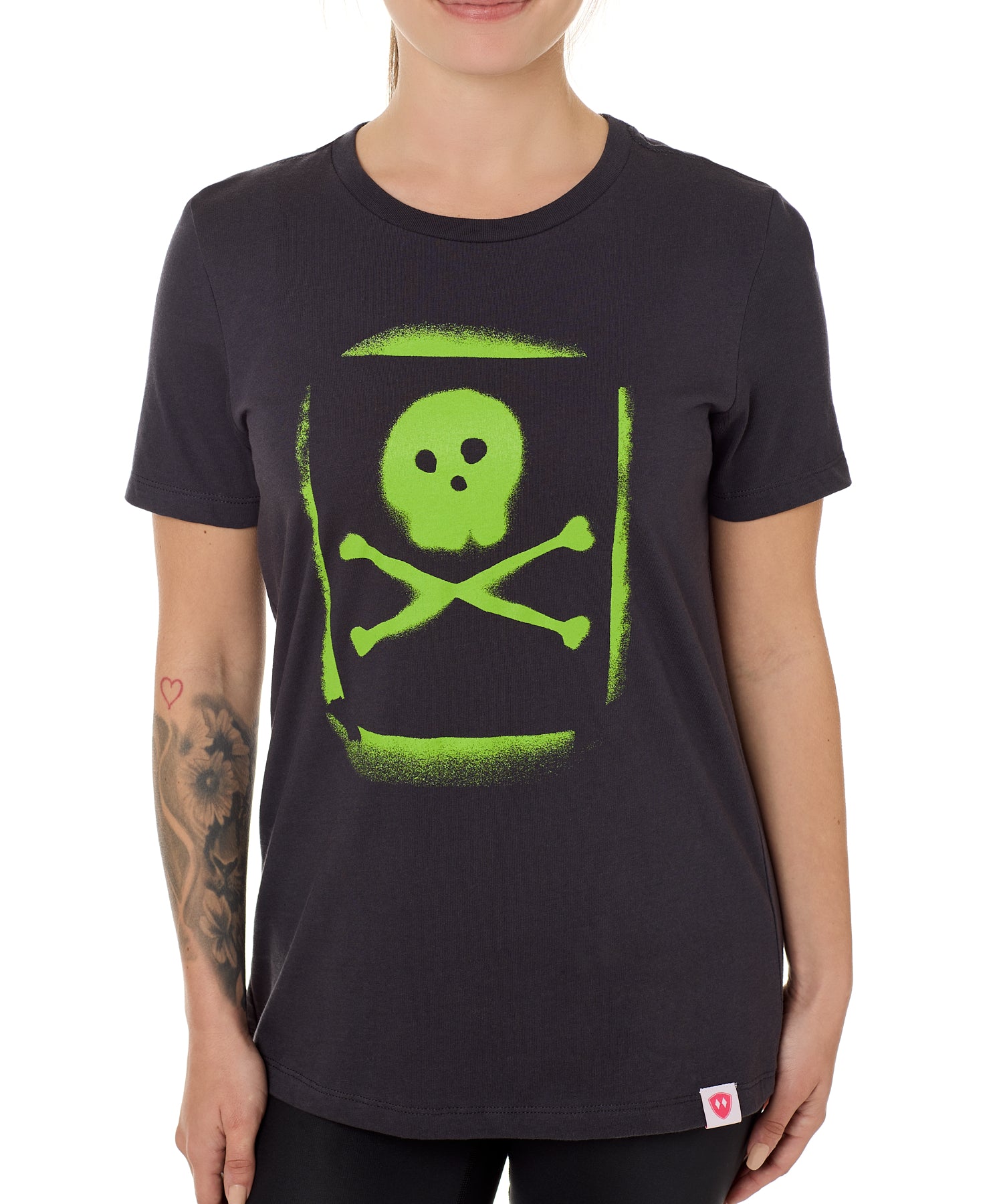 A woman wearing a black crew neck t-shirt with a green spray-painted skull and crossbones graphic on the front.