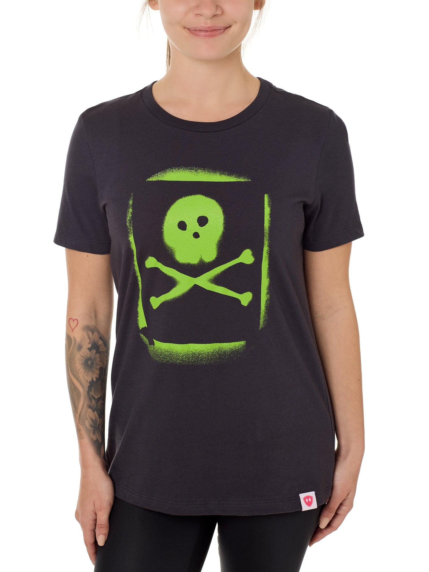 A woman wearing a black crew neck t-shirt with a green spray-painted skull and crossbones graphic on the front.
