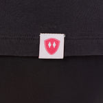 Close-up detail of a pink Double Diamond Shield woven hem label on a dark gray tee shirt.