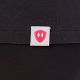 Close-up detail of a pink Double Diamond Shield woven hem label on a dark gray tee shirt.
