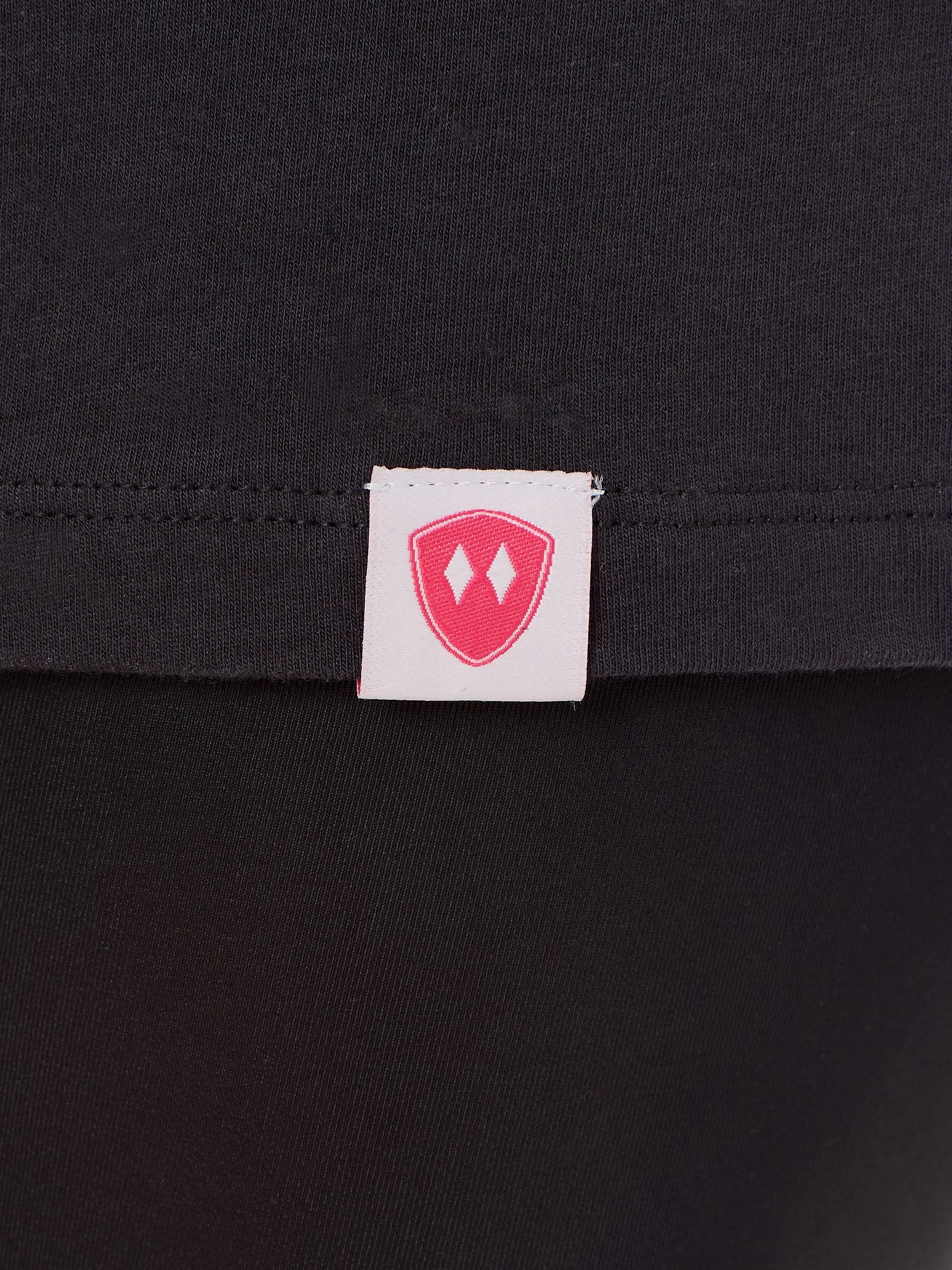 Close-up detail of a pink Double Diamond Shield woven hem label on a dark gray tee shirt.