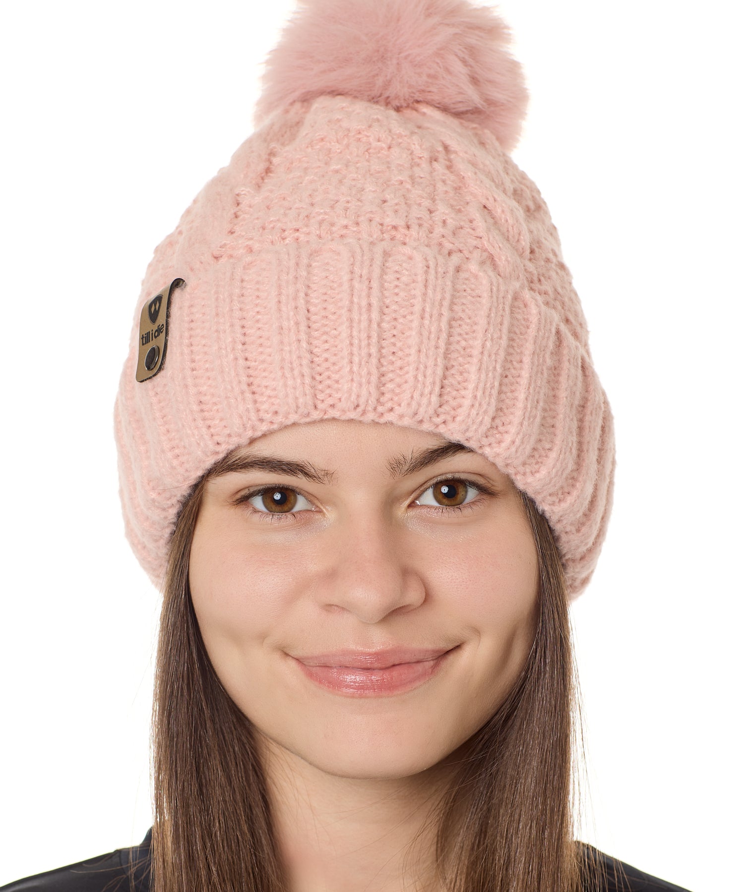 front view of a female model wearing a blush knit pom beanie featuring a matching pom pom, cuff and leather till i die logo tab with a nickel fastener.