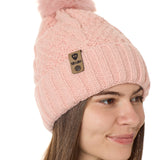 side view of a female model wearing a blush knit pom beanie featuring a matching pom pom, cuff and leather till i die logo tab with a nickel fastener.