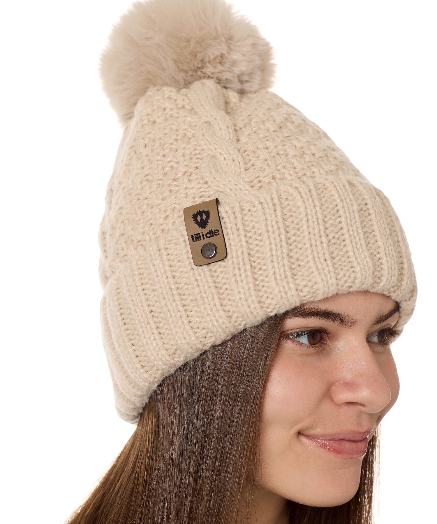 side view of a female model wearing a vintage white knit pom beanie featuring a matching pom pom, cuff and leather till i die logo tab with a nickel fastener.