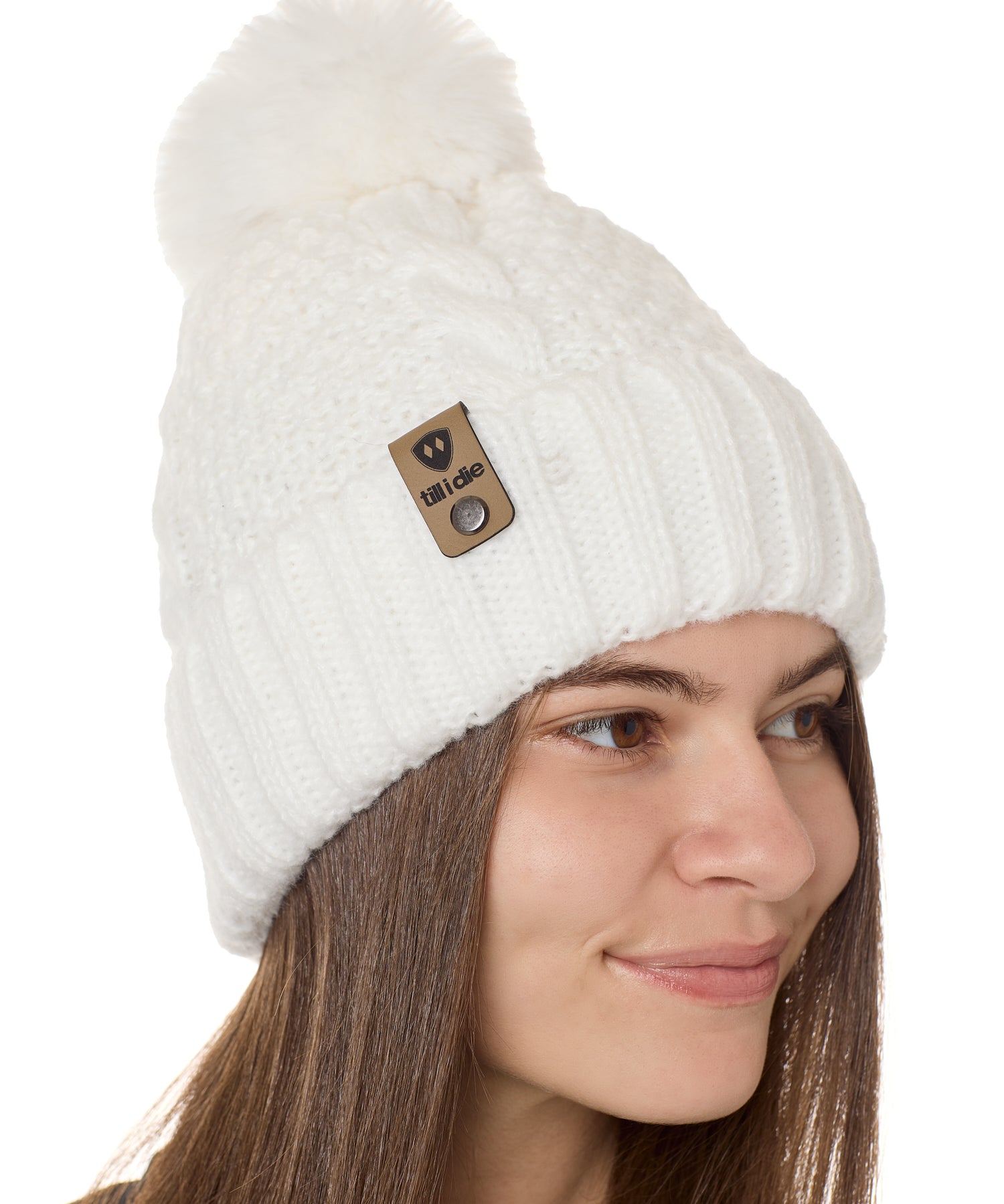 side view of a female model wearing a white knit pom beanie featuring a matching pom pom, cuff and leather till i die logo tab with a nickel fastener.