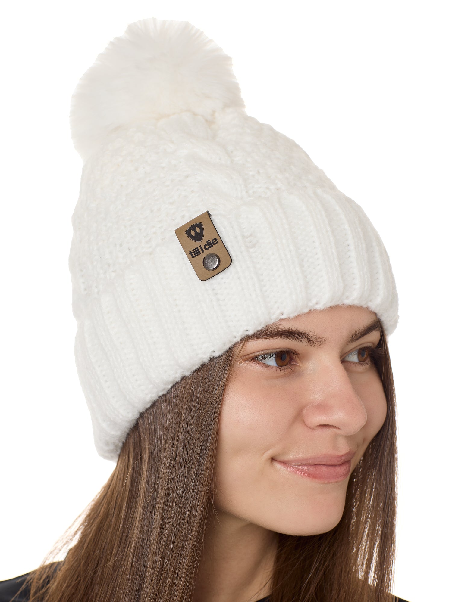 side view of a female model wearing a white knit pom beanie featuring a matching pom pom, cuff and leather till i die logo tab with a nickel fastener.