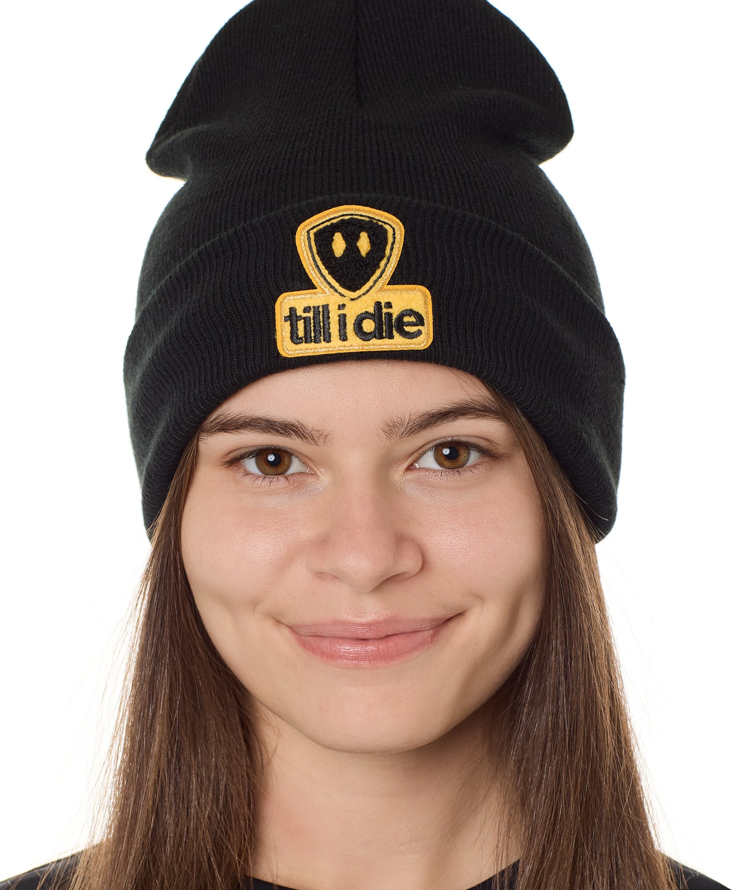 A person wearing a black beanie with a 'Till I Die' logo chenille patch on the front.