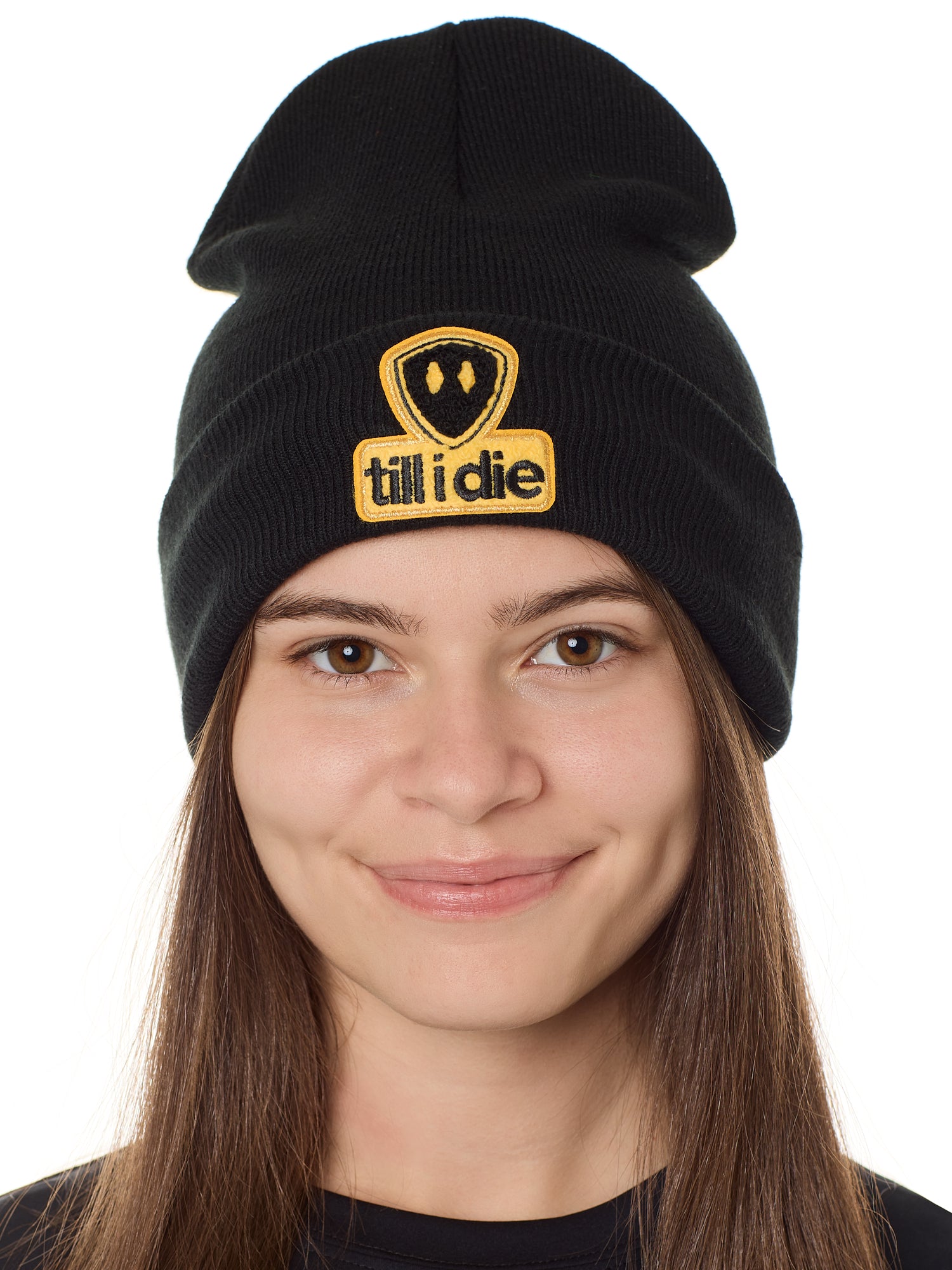 A person wearing a black beanie with a 'Till I Die' logo chenille patch on the front.