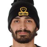 Front view of a male model wearing a black knit beanie, featuring a cuff and a chenille patch of the Till I Die logo in yellow and black.