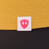 Close-up detail of a pink Double Diamond Shield woven hem label on a mustard tee shirt.