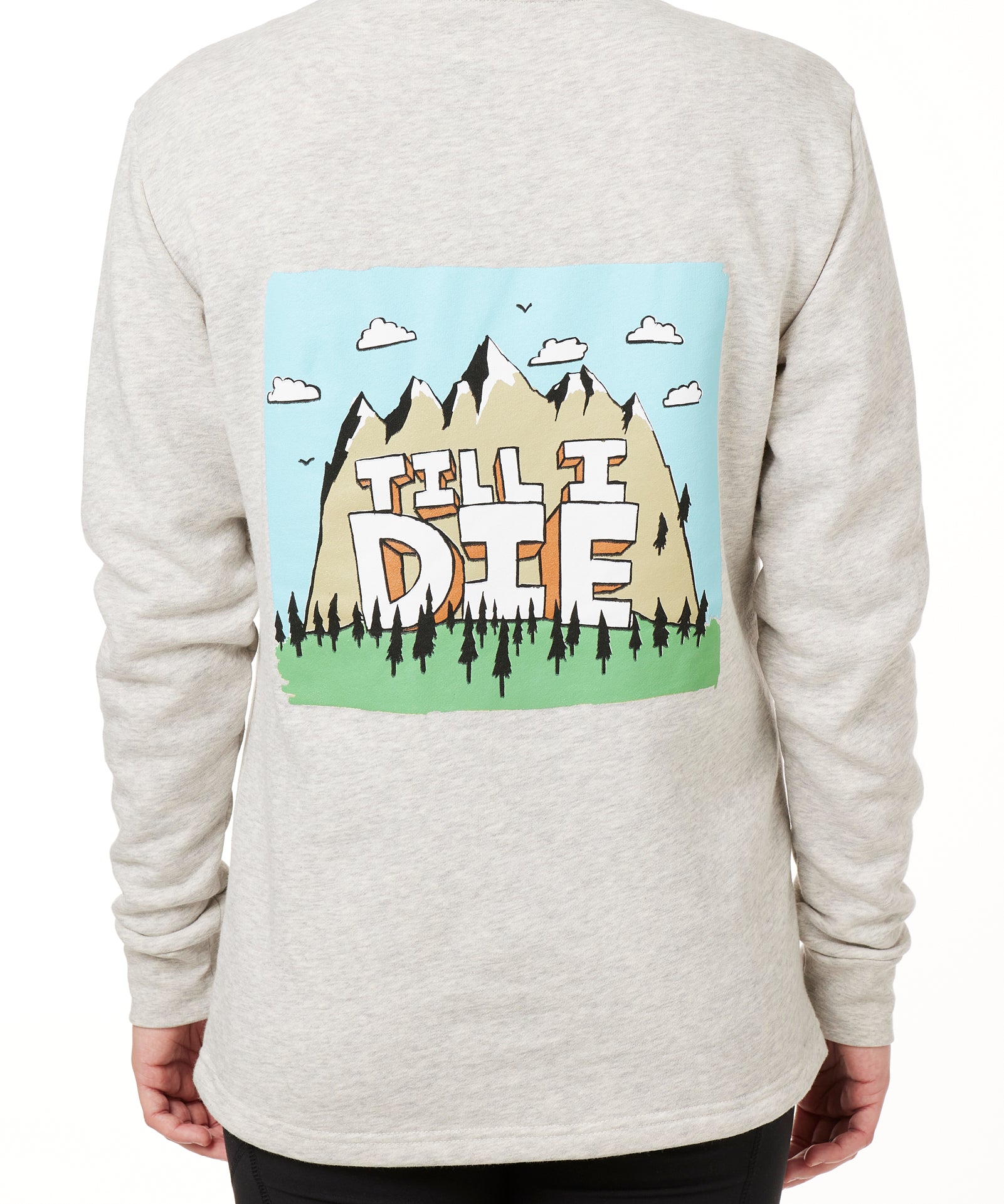 FEMALE MODEL WEARING A HEATHER OATMEAL HOODIE WITH HOOD UP, FEATURING A GRAPHIC OF A CARTOON MOUNTAIN THAT HAS TILL I DIE ACROSS IT