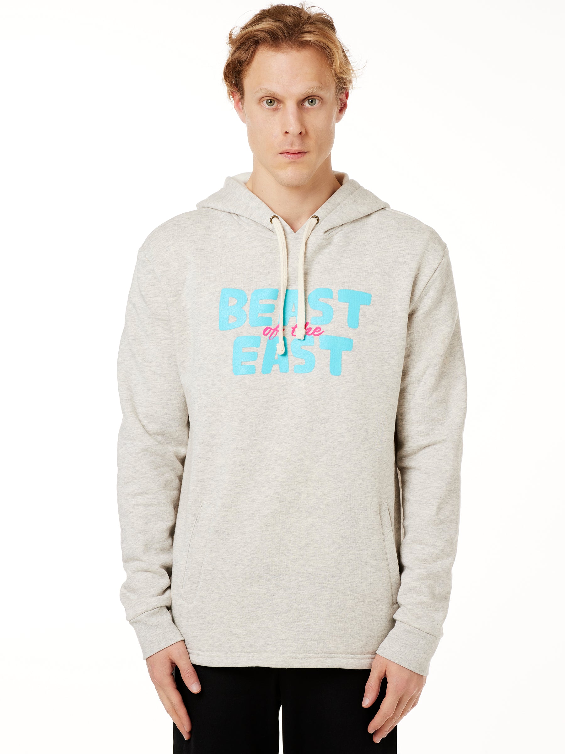 FEMALE MODEL WEARING A HEATHER OATMEAL HOODIE WITH A PINK AND BLUE GRAHIC THAT SAYS BEAST OF THE EAST