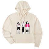 Cream women’s cropped hoodie featuring an illustrated trio of female skiers dressed in retro 1980s ski fashion, rendered in black and white with bold hot pink accents.
