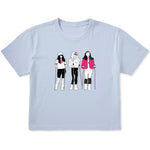 Light blue women’s cropped T-shirt featuring an illustrated trio of female skiers dressed in retro 1980s ski fashion, rendered in black and white with bold hot pink accents.