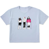 Light blue women’s cropped T-shirt featuring an illustrated trio of female skiers dressed in retro 1980s ski fashion, rendered in black and white with bold hot pink accents.