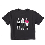 Black women’s cropped T-shirt featuring an illustrated trio of female skiers dressed in retro 1980s ski fashion, rendered in black and white with bold hot pink accents.