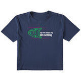 Navy short sleeve crop T-shirt featuring a neon green technical illustration of a ski binding with hot pink accents and a DIN setting cranked to 11, alongside bold white text reading, “Ask me about my DIN setting.”