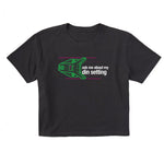 Black short sleeve crop T-shirt featuring a neon green technical illustration of a ski binding with hot pink accents and a DIN setting cranked to 11, alongside bold white text reading, “Ask me about my DIN setting.”