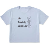 Light blue cropped T-shirt featuring black text and hand-drawn icons celebrating three mountain essentials: pie, French fries, and “Ski Till I Die,” finished with the signature Double Diamond shield.