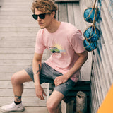 Male model in a beach town setting, sitting on the boardwalk wearing the surf truck tee and smoke and mirrors sunglasses
