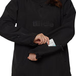 Mid-frame shot showing model accessing lift-pass pocket on left sleeve of black pullover hoodie.