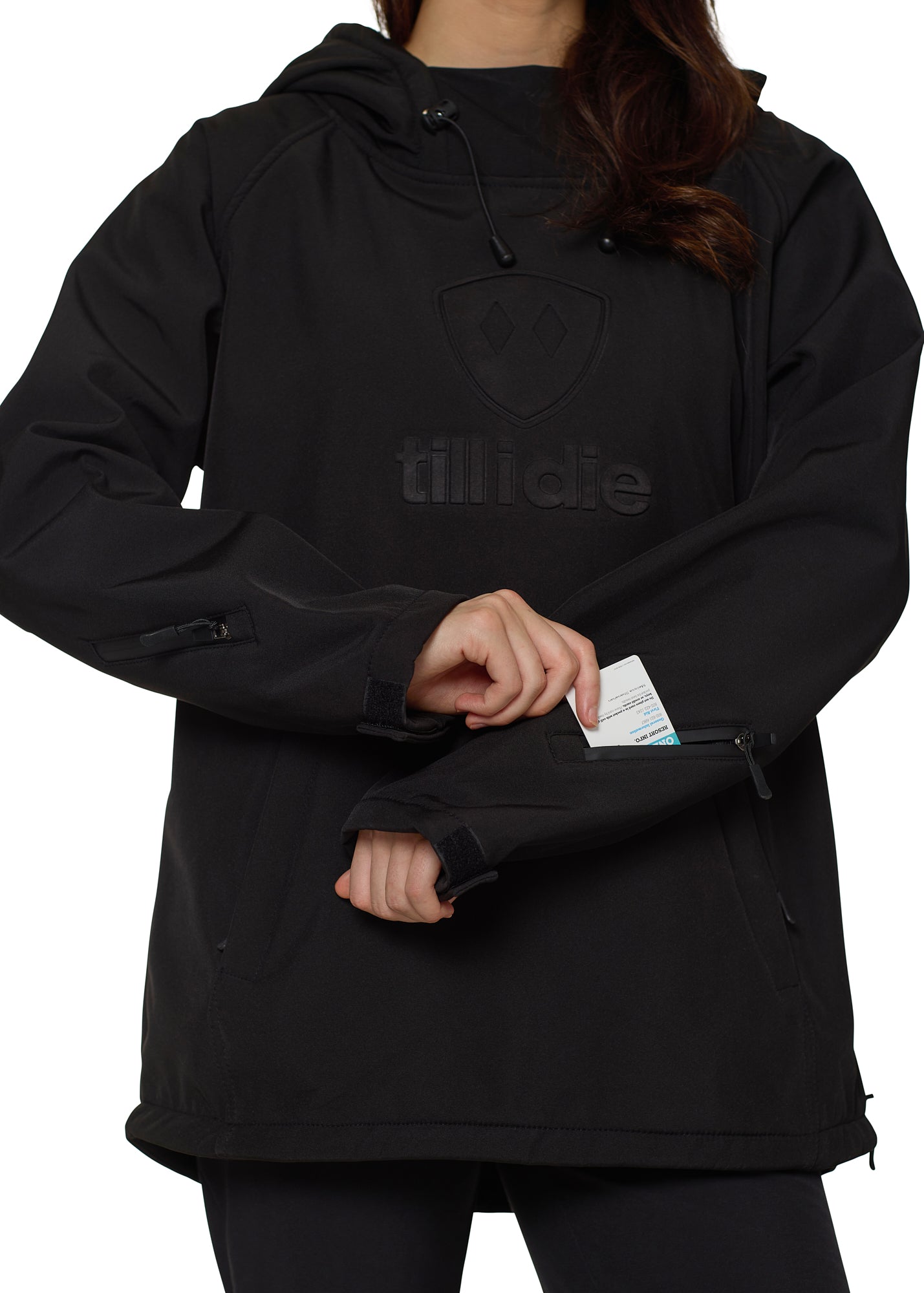 Mid-frame shot showing model accessing lift-pass pocket on left sleeve of black pullover hoodie.