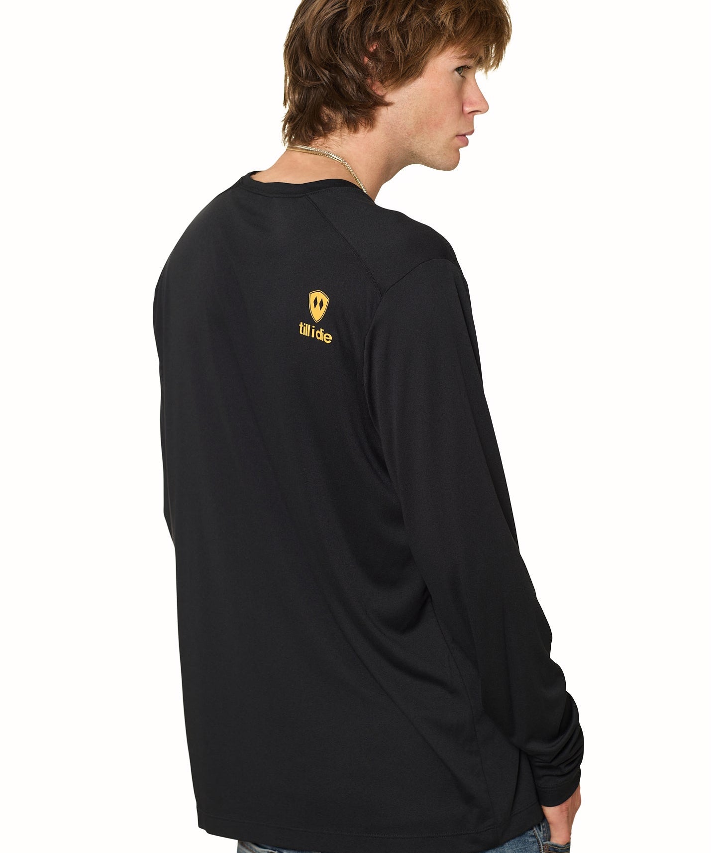 Back view of male model wearing black long sleeve featuring orange Till I Die logo and double diamond shield on shoulder