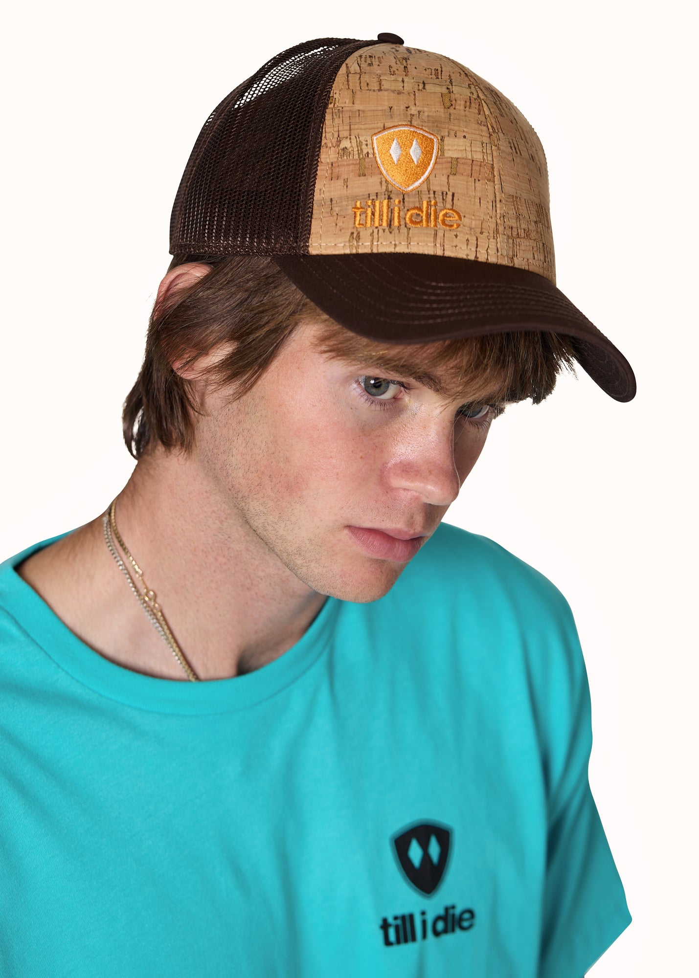 male model wearing a brown cork trucker hat with an orange embroidered till i die logo