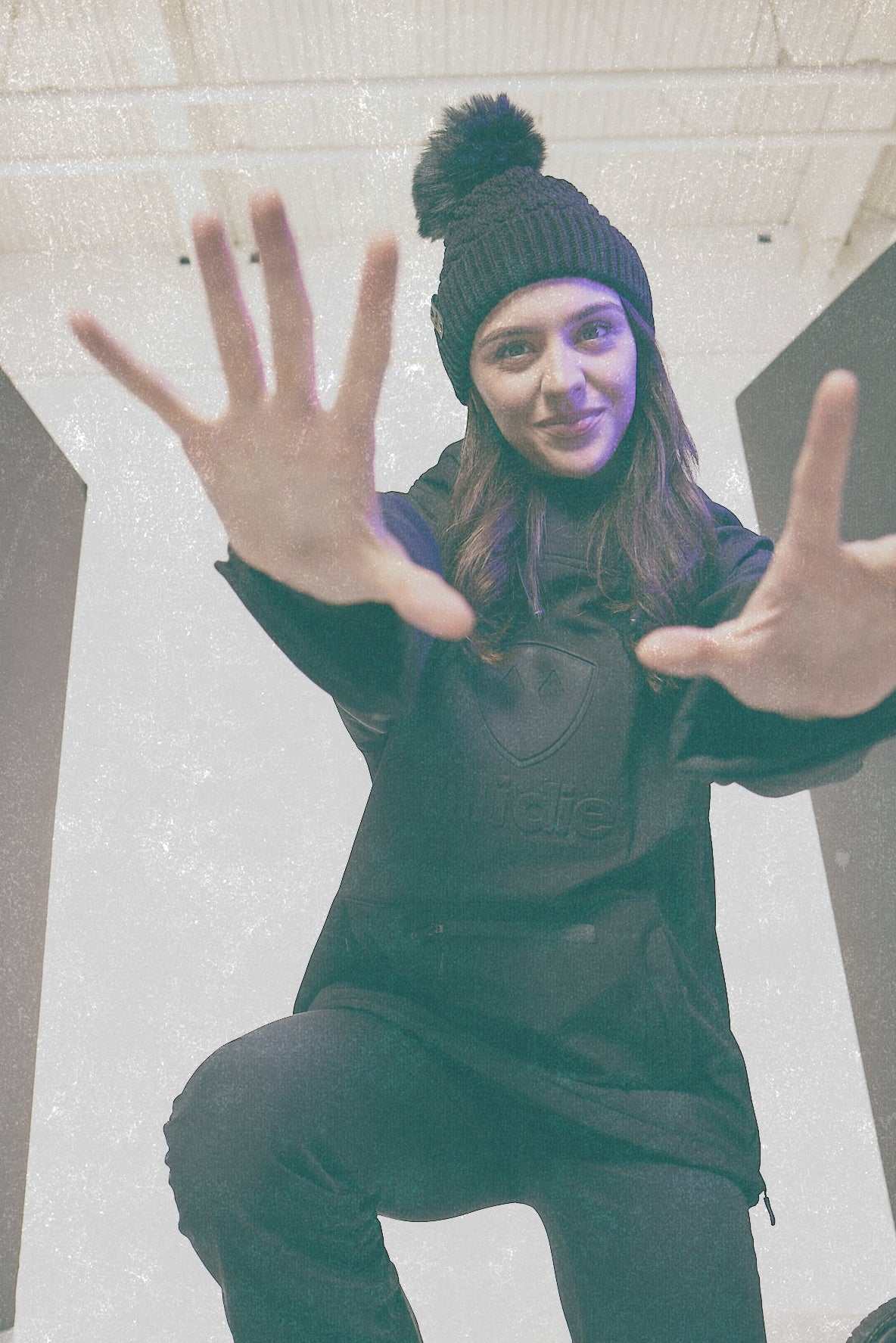 Person wearing a black beanie and jacket with hands outstretched in a neutral setting