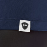 Close-up detail of a black Double Diamond Shield woven hem label on a navy performance long sleeve shirt.