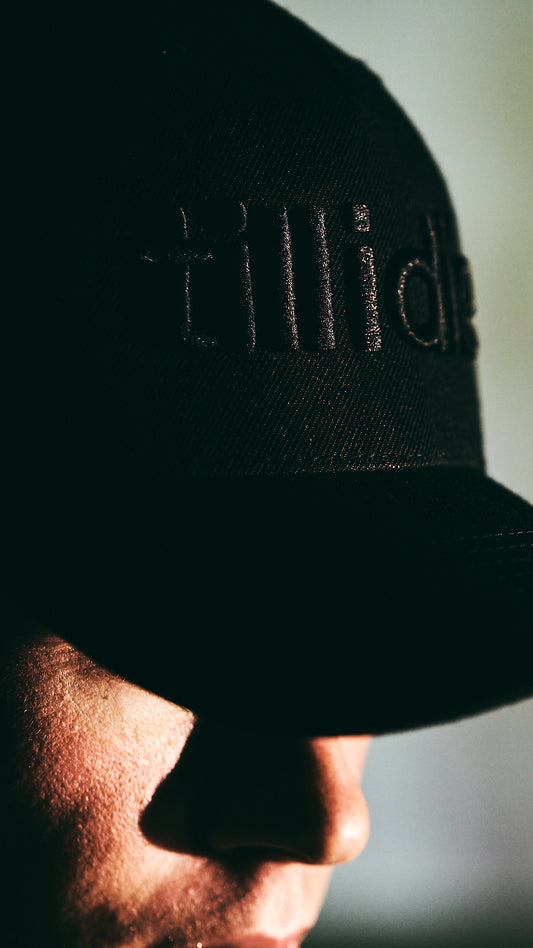 Close-up view of a male model wearing the black Till I Die puffer hat. The scene is moody, with dramatic lighting adding depth and texture.